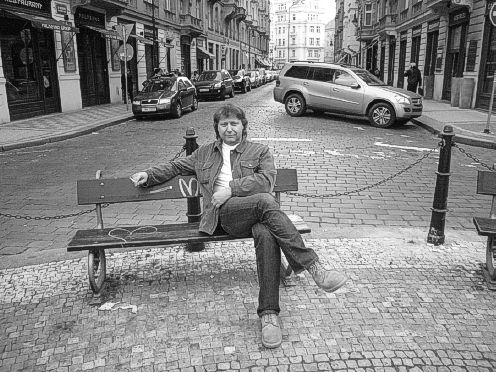 Helmut Fröschl sitzt mit einer Gitarre auf einer Bank