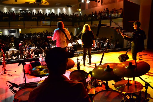Blick von der Bühne über die Band in den gefüllten Konzertsaal